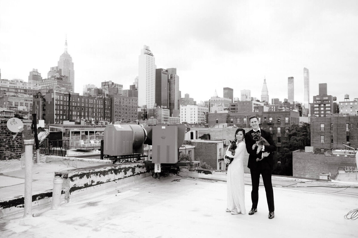 The bride and the groom are carrying their dogs on a rooftop, with many buildings in the background, in NYC. Image by Jenny Fu