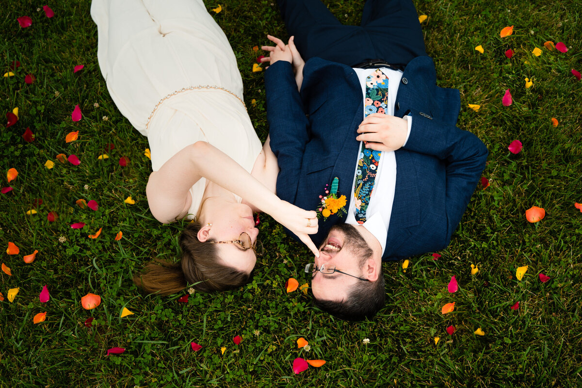 A wedding couple laying down in the grass as one touches the other's nose.