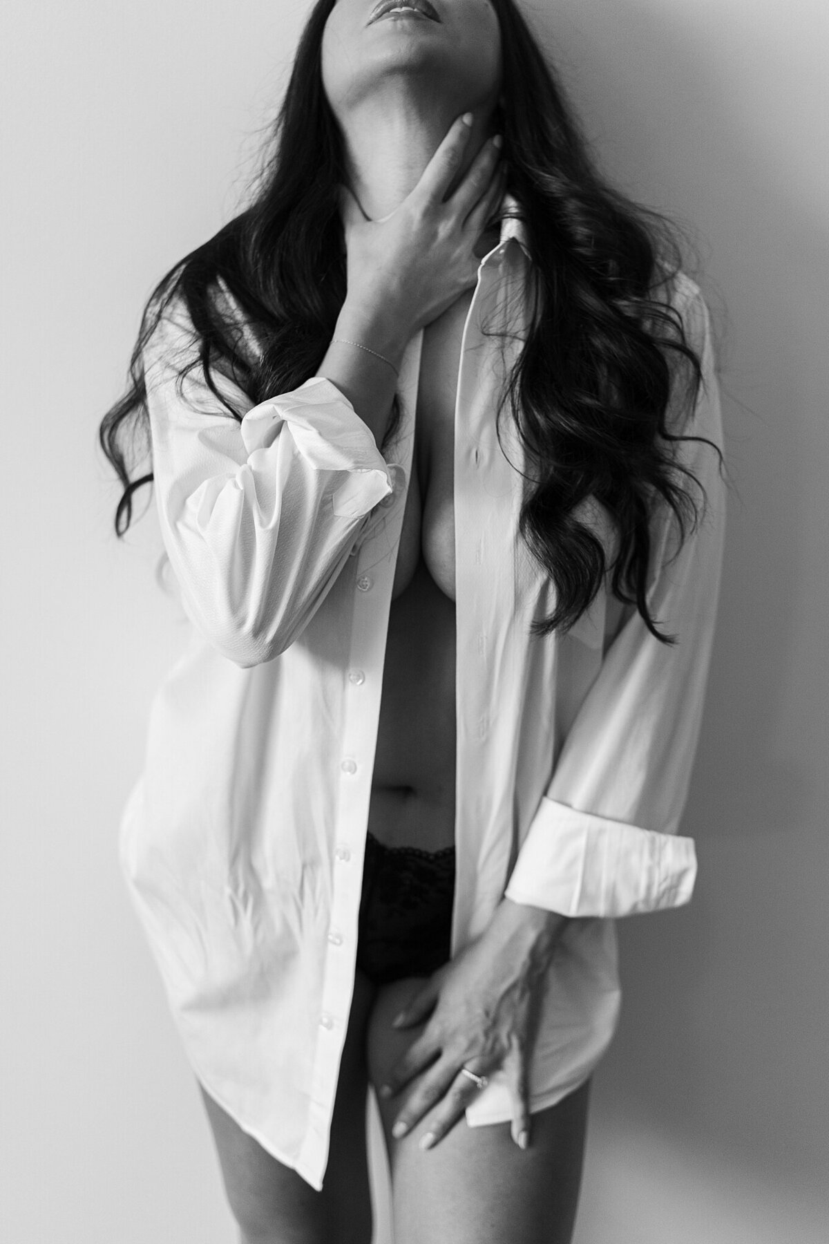 Woman wearing partners white button down shirt with just a slight amount of cleavage showing in detroit boudoir studio.