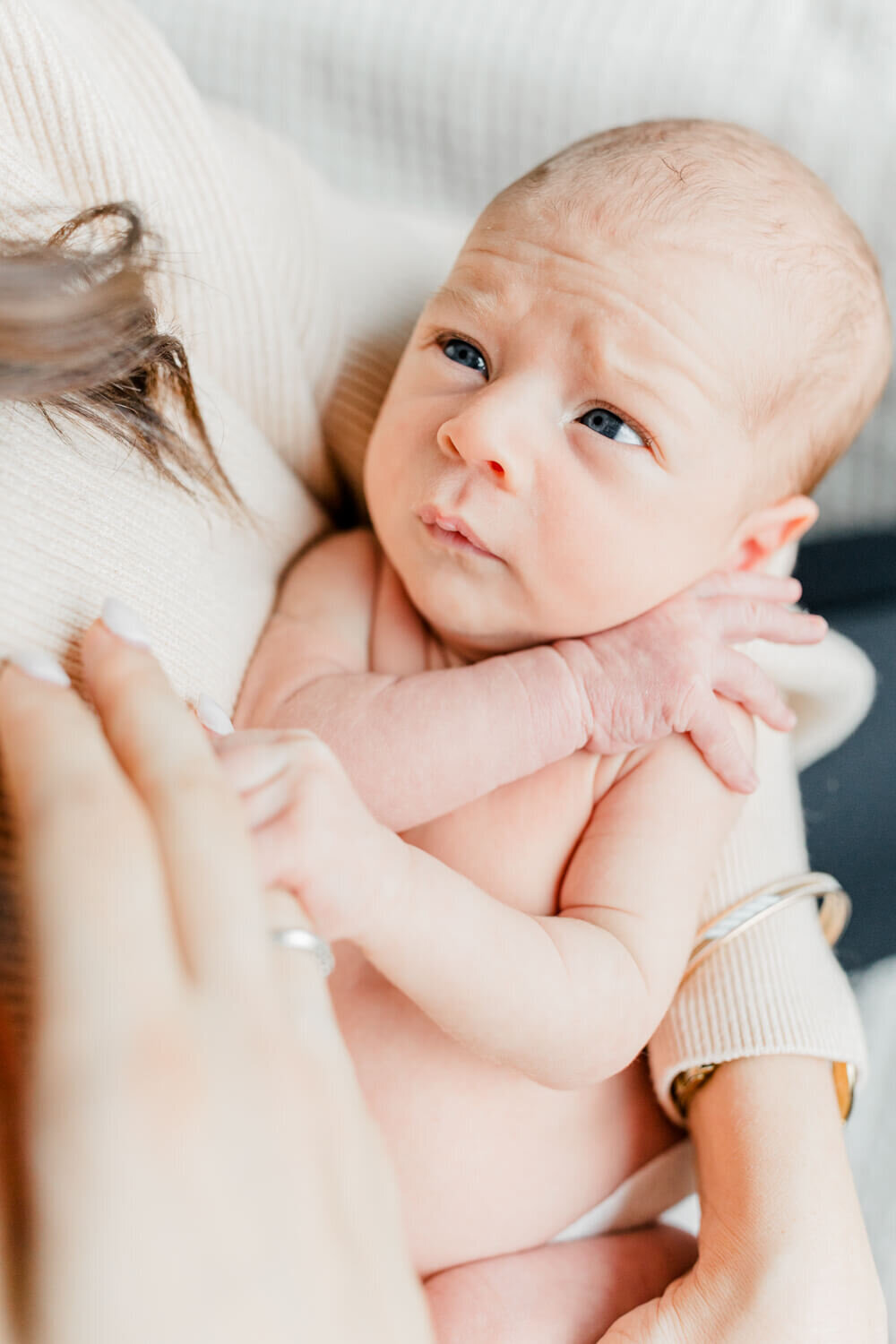 Newborn baby looking up at his mother and grasping her finger