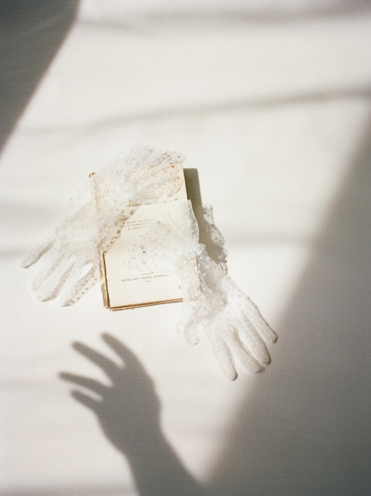 ethereal, mystical film flat lay, directional light, antique book, tulle gloves with pearls, hand shadow reaching