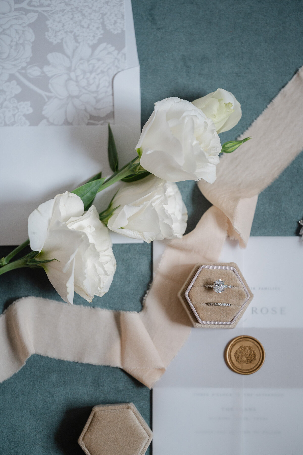 a flat lay with white roses, ribbon, wedding rings, and wedding invitations