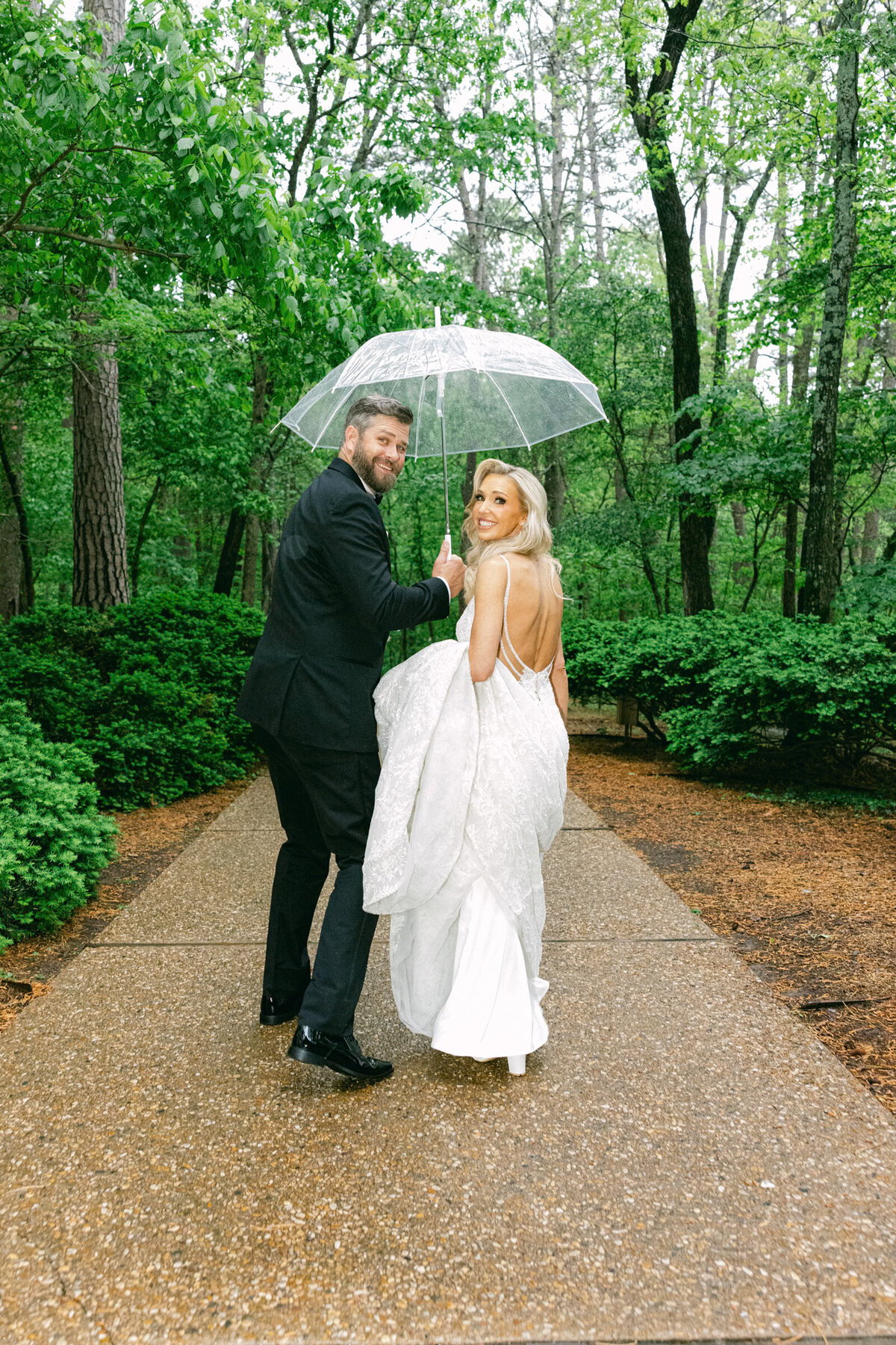 A wedding day photo of the bride and groom walking under an umbrella after their ceremony