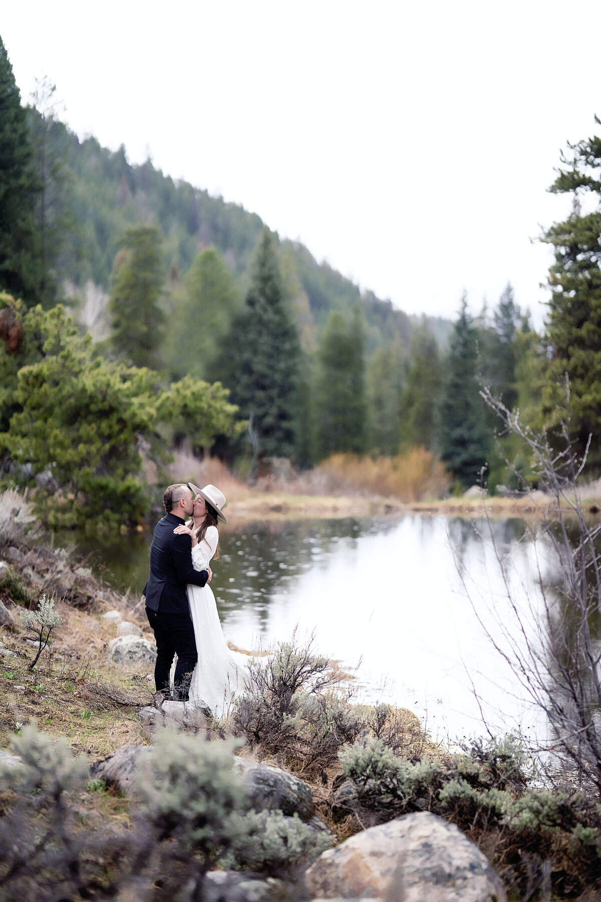 Bride and groom kissing and hugging by the lake at Beyul Retreat, in their Aspen Colorado wedding,
