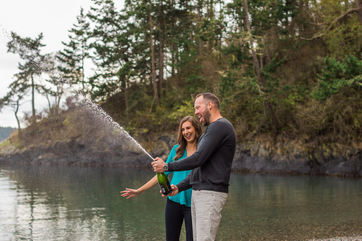 Fun PNW Seattle nature engagement session by Puget Sound couple popping champagne and laughing photo by Joanna Monger Photography