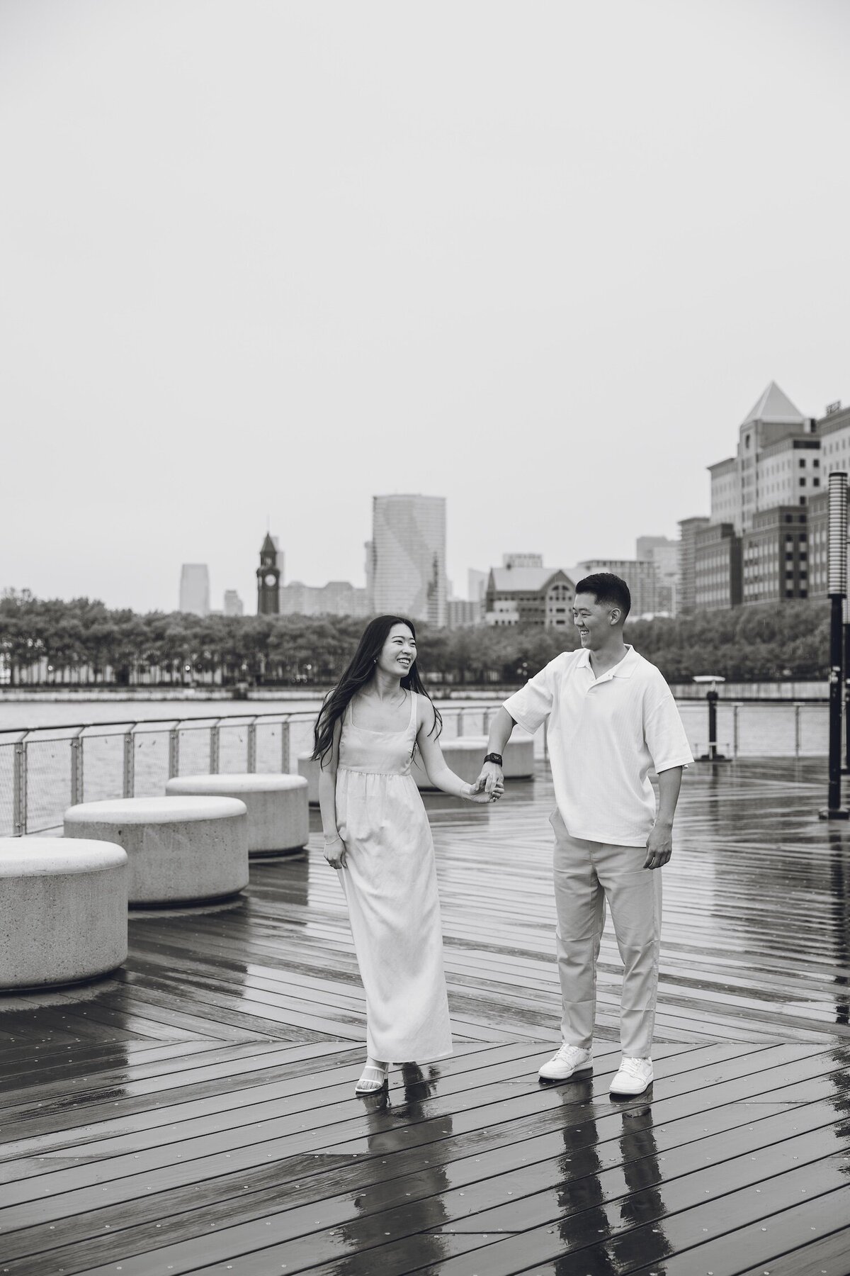 Black and white photo of couple walking on rainy waterfront boardwalk