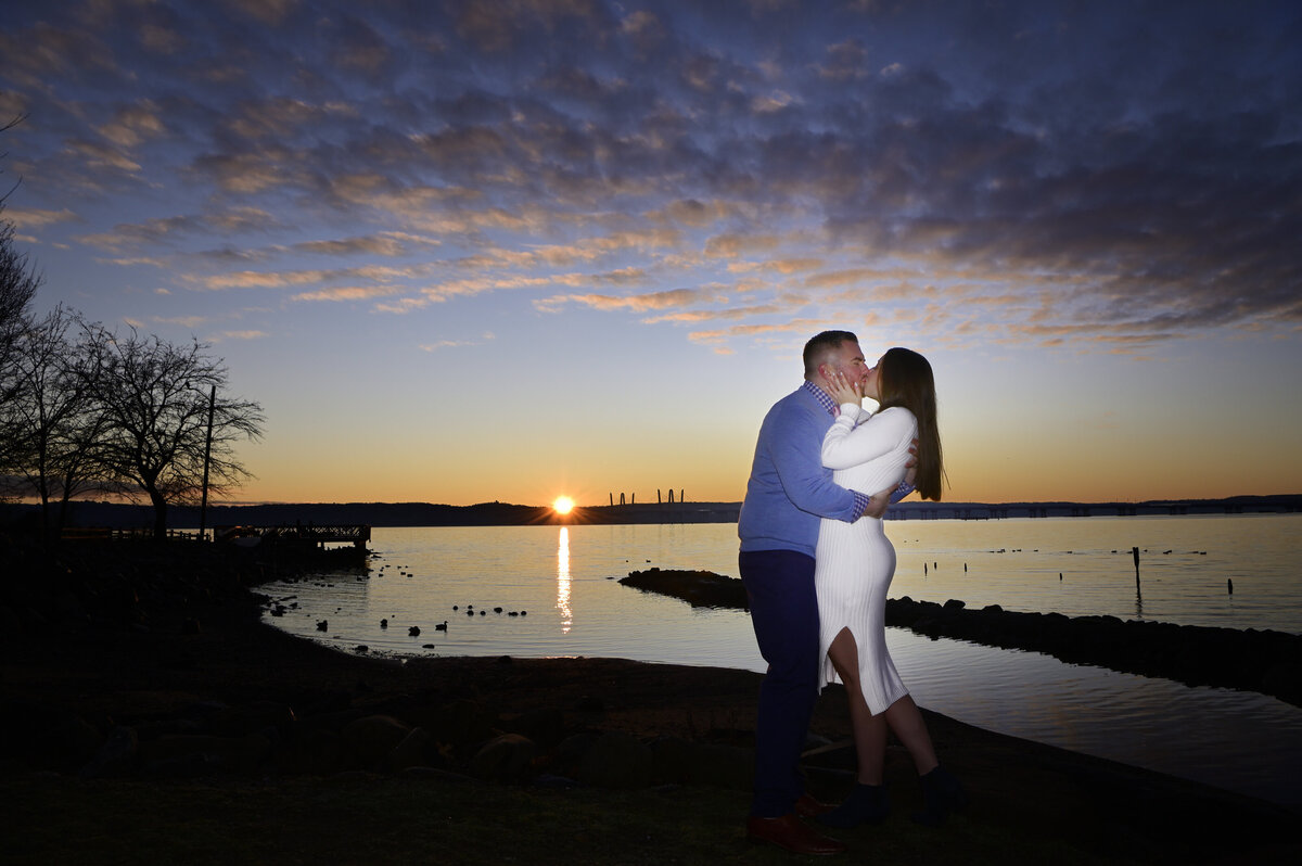 A couple kissing at sunrise on the edge of the water 
