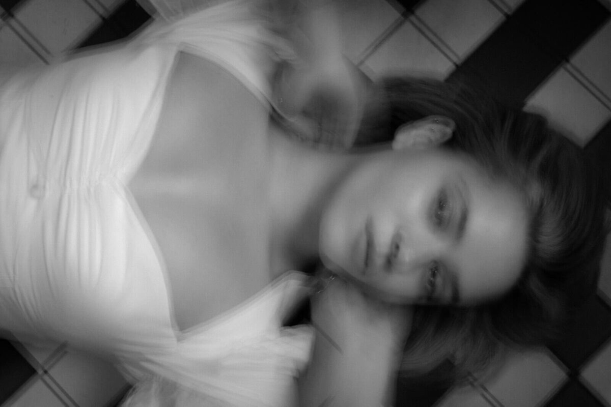 A bride lay on the floor in a white dress, looking at the camera. The image is blurred artistically