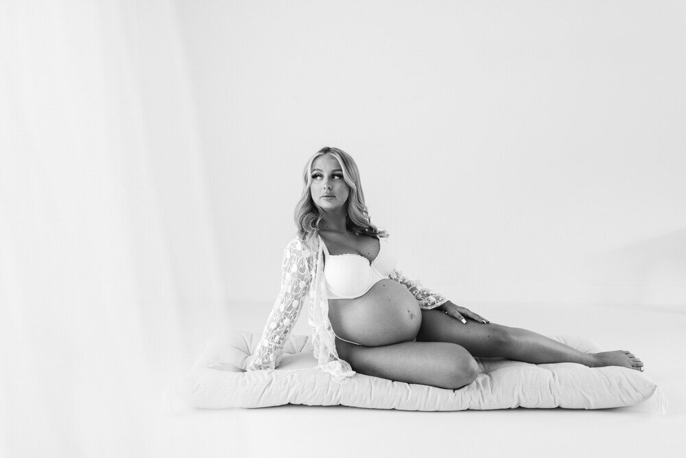 Pregnant woman lounges on a floor cushion whilst looking out of the window and poses for a photo