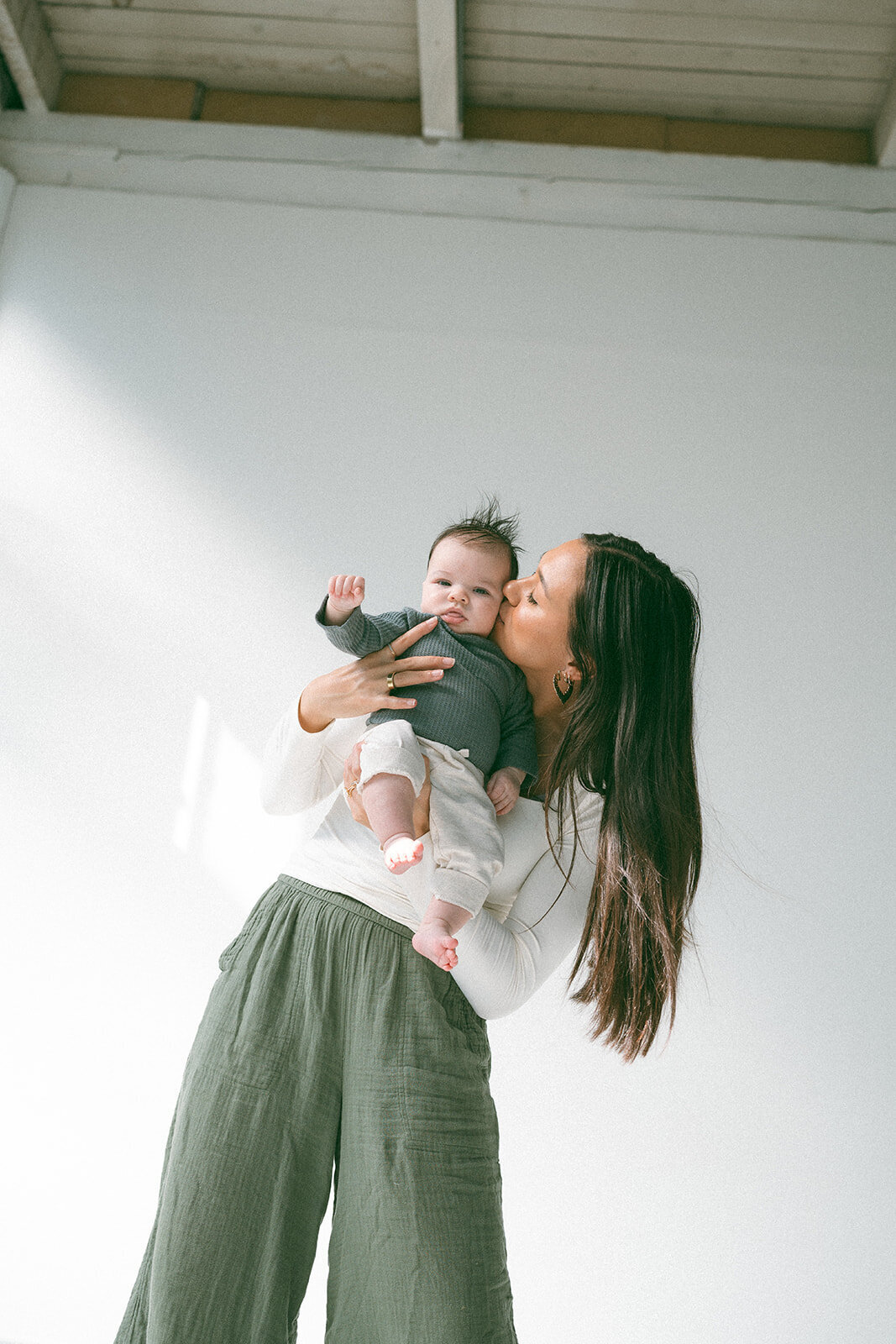 Tender newborn photo in Orange County with mother lifting baby and giving a kiss.