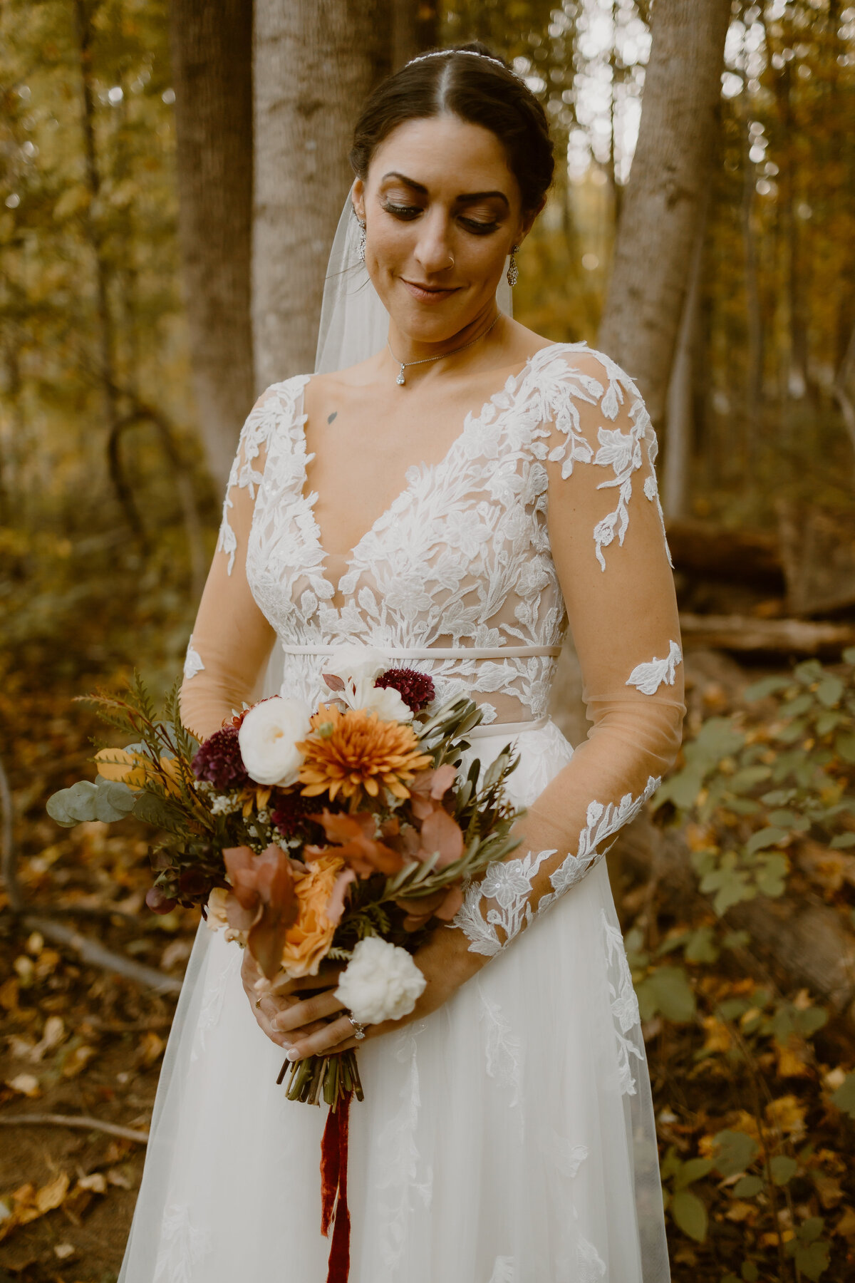 A bride stands in an autumn forest while holding flowers
