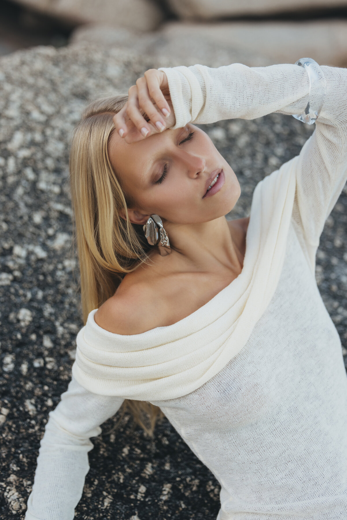 Model Johanna leunt ontspannen tegen een rots in Kaapstad, met ogen gesloten en een off-shoulder witte jurk bij zonsopgang.