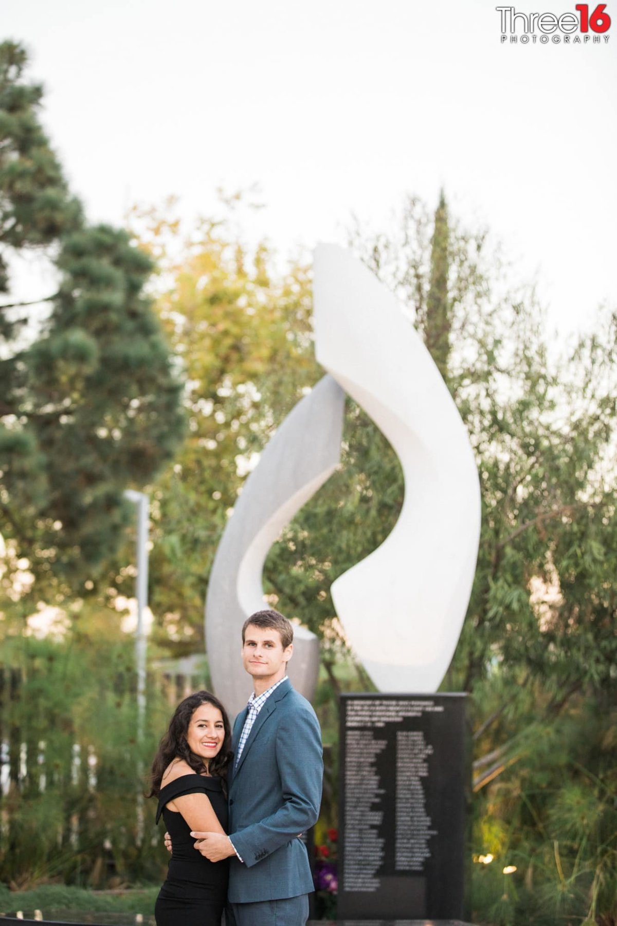 Engaged couple pose for engagement photos in front of a sculpture