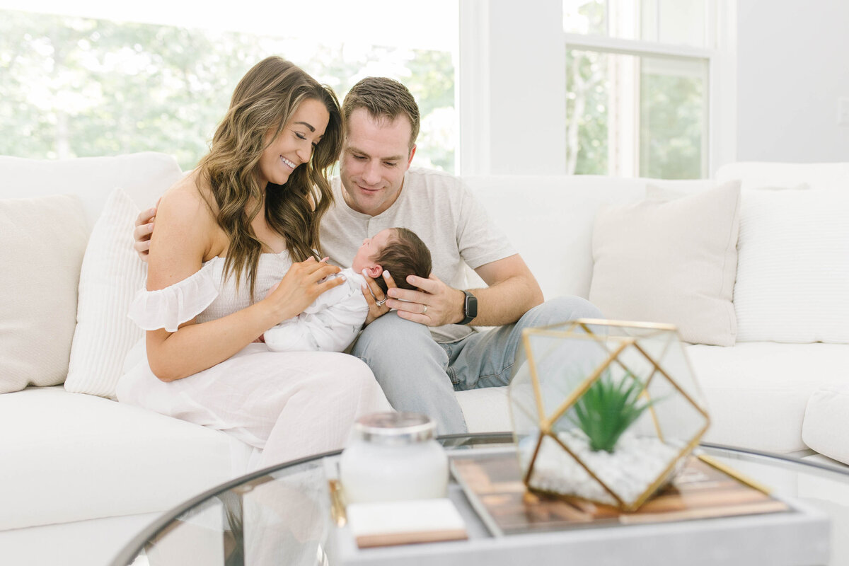 happy parents smiling at newborn baby boy on couch