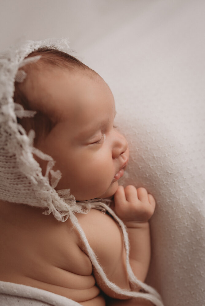 Newborn photo shoot photographed by Atlanta, Georgia newborn photographer with baby posing on neutral fabric with dainty headband on and sleeping. Up close shot looking down on baby.
