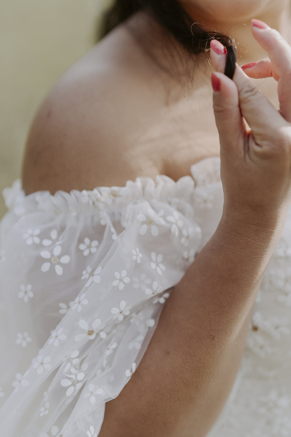 bride's white dress off shoulder and her red nails twirling her hair