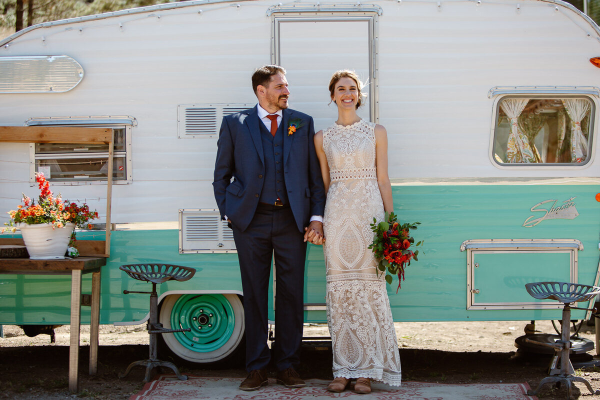 Two marriers hold hands in front of a vintage RV.