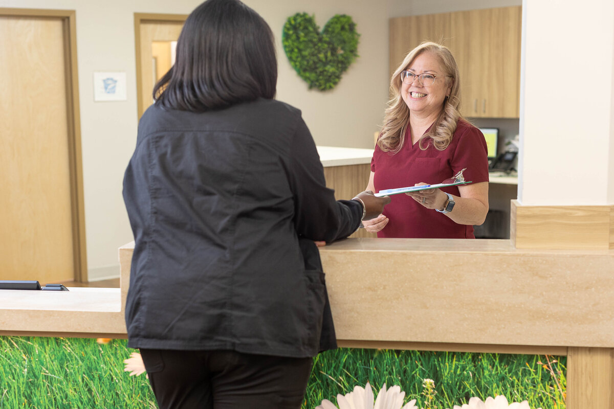 smiling receptionist handing an incoming patient a clipboard