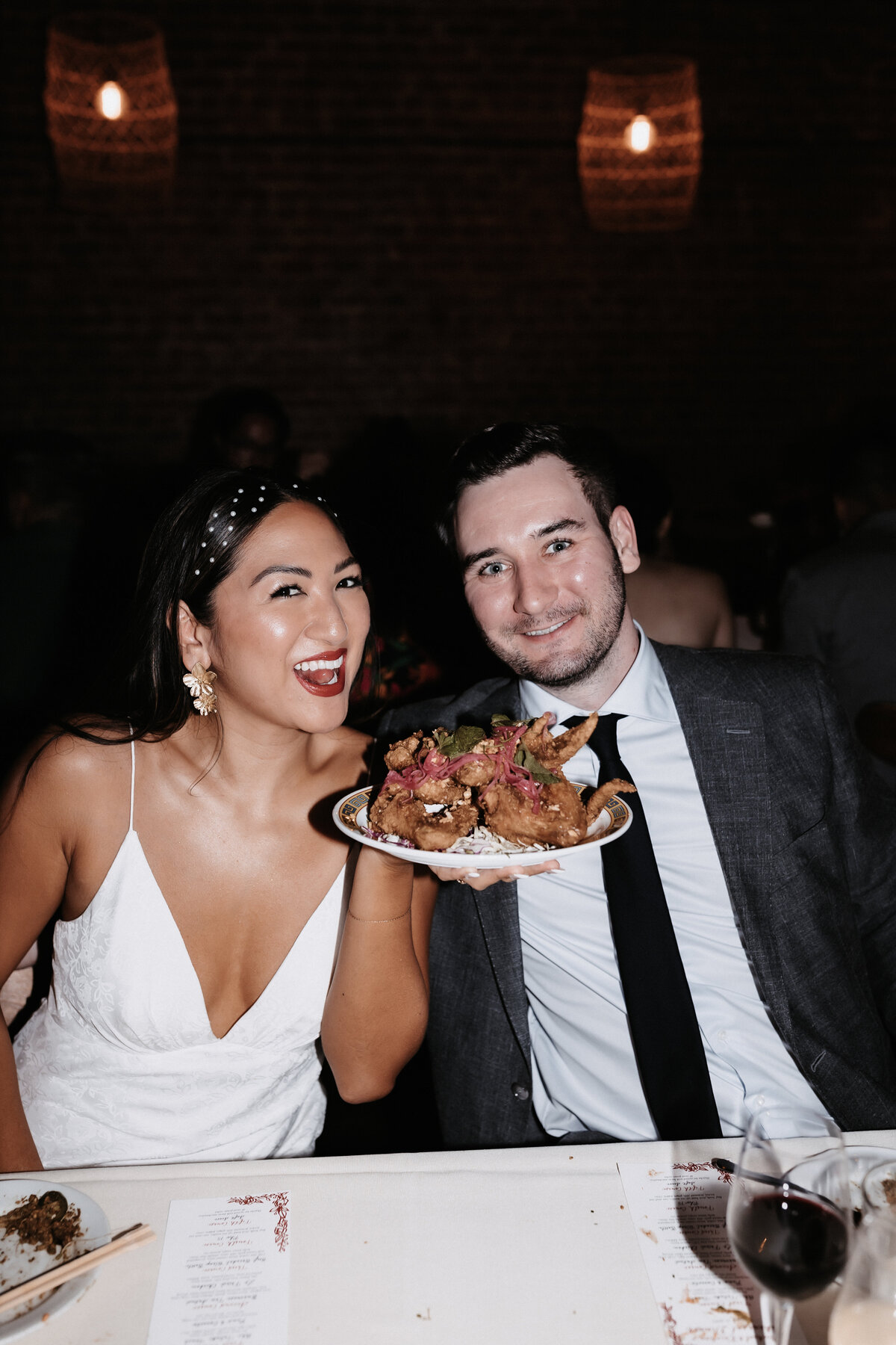 Bride and groom holding up plate of food smiling at restaurant