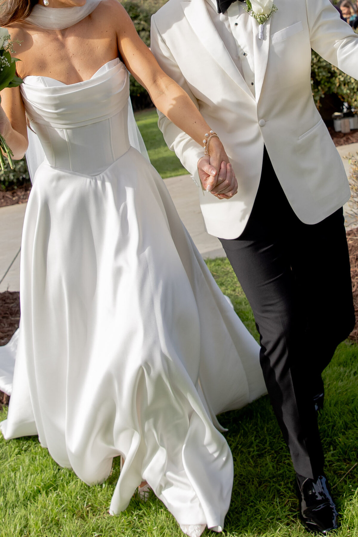 A bride and groom run while holding hands on their wedding day. The photo is cropped so you don't see their faces.