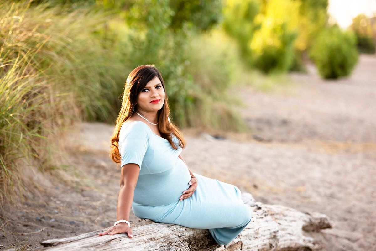 Pregnant woman sitting on a log on the beach for her outdoor beach maternity photography session in Burlington, ON