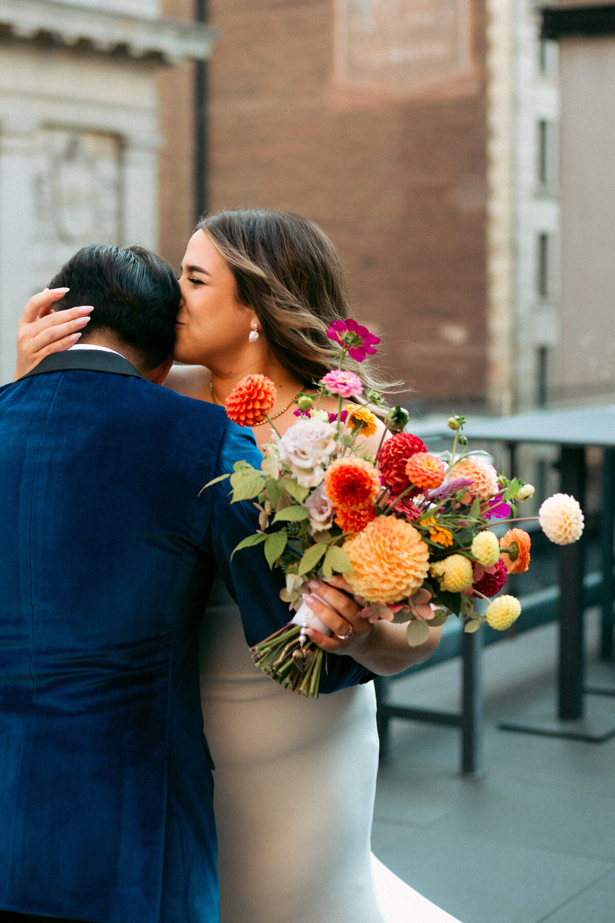 Bride holding a bright bouquet kisses the groom playfully on a street in Old Montreal. 