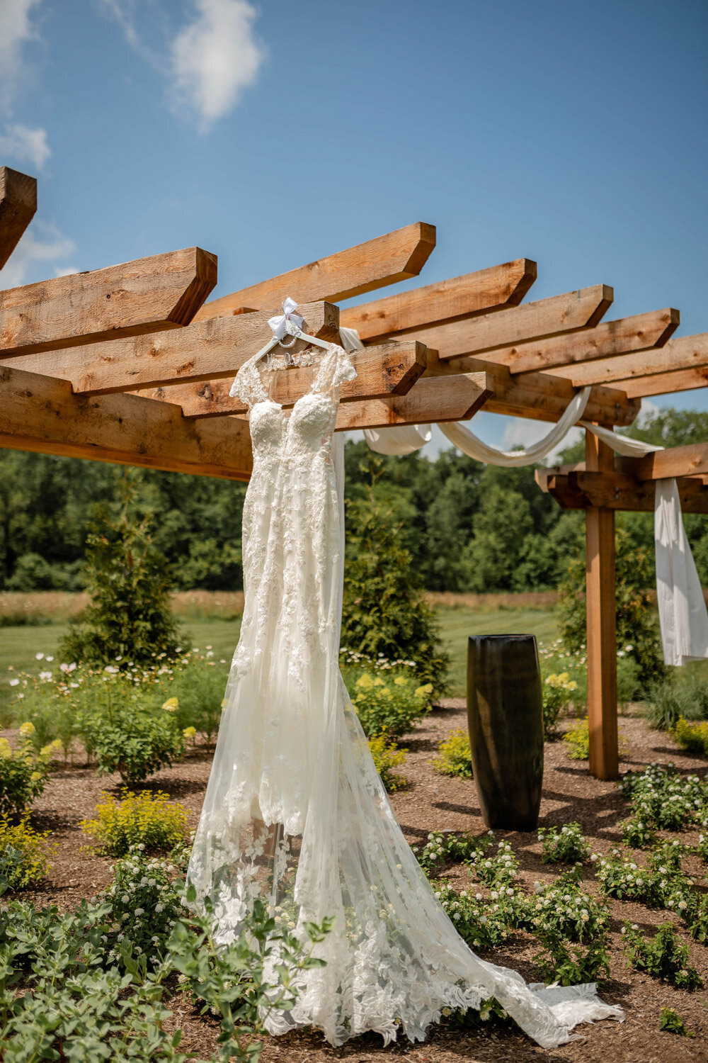 Wedding dress hanging from the wooden pergola surrounded by greenery
