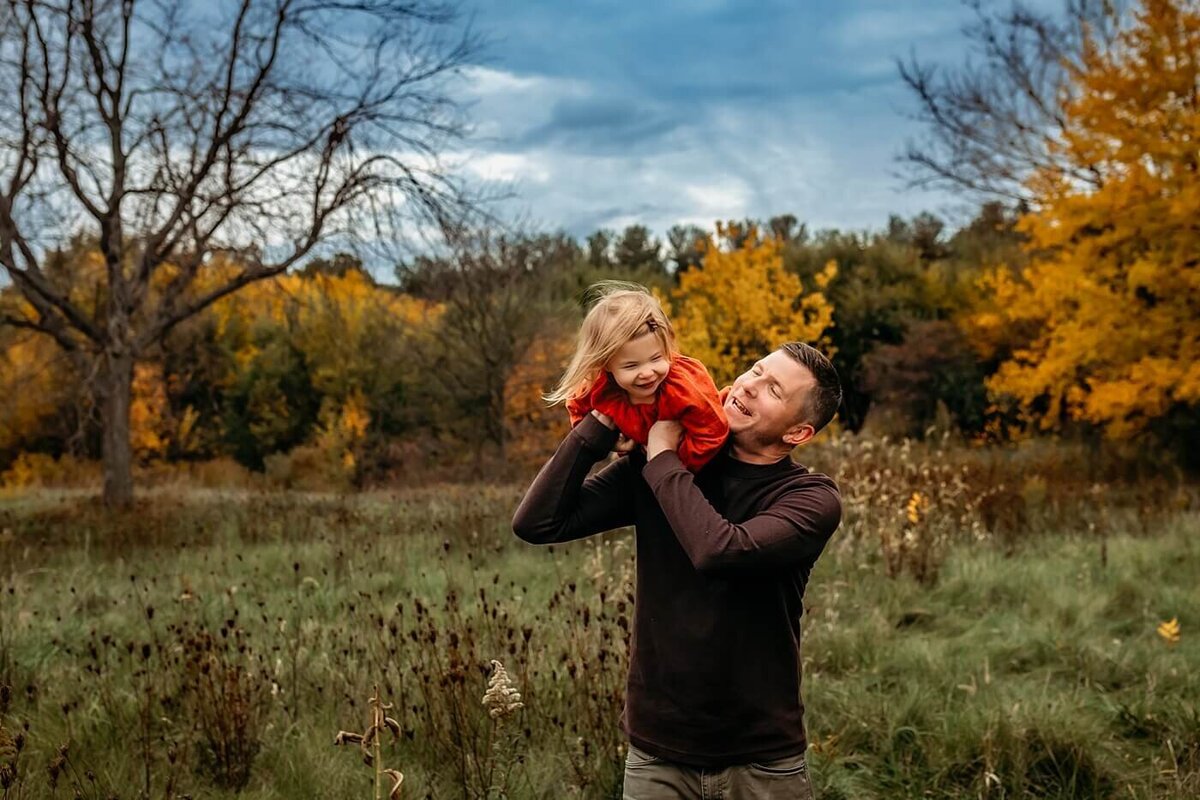 Family photography session with fall colors of dad and little girl standing in a grassy field being playful in Bloomington/Normal, Illinois