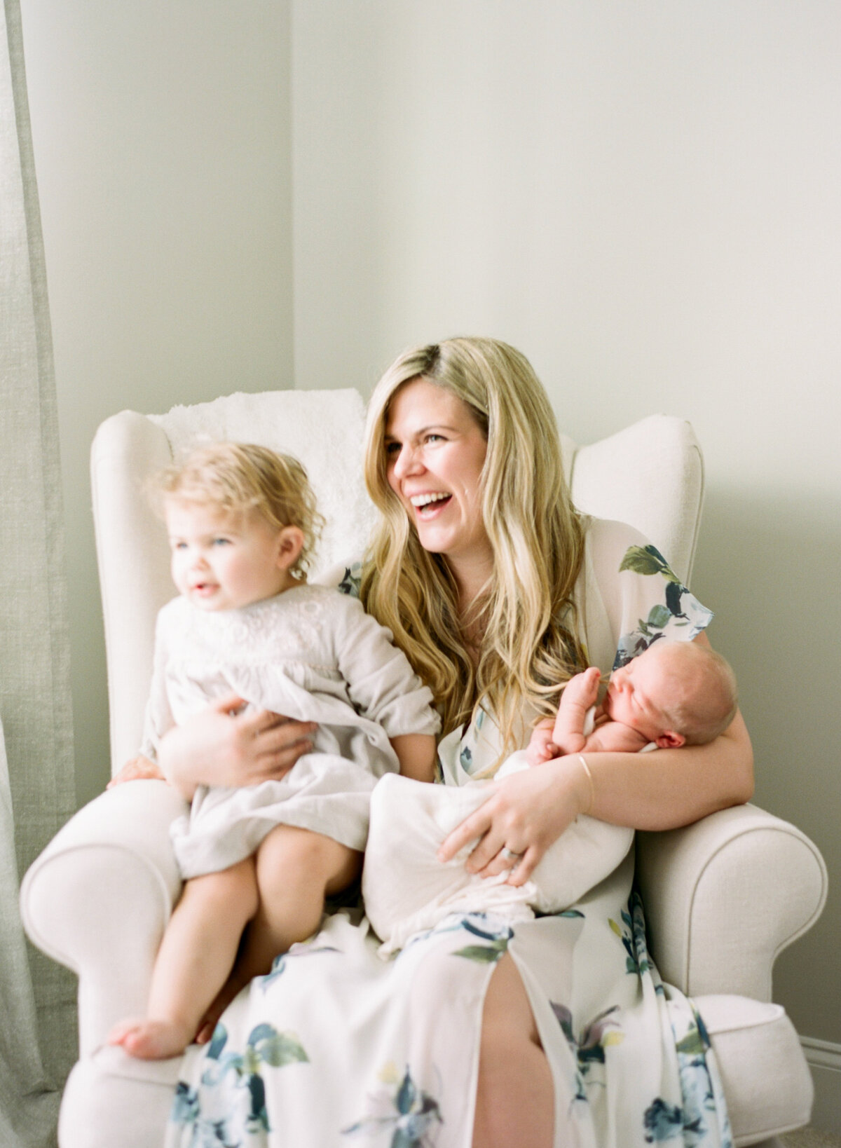 Mom laughs as she holds her toddler and baby during her in home newborn session in Cary N C. Image by Raleigh newborn photographer A.J. Dunlap Photography.