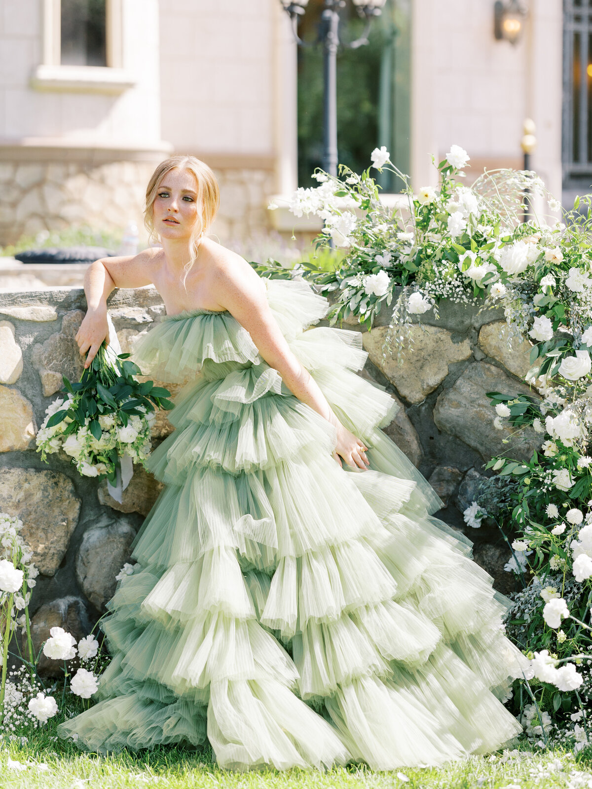 bride stands in editorial green ruffle gown with white and green flowers around her in Utah