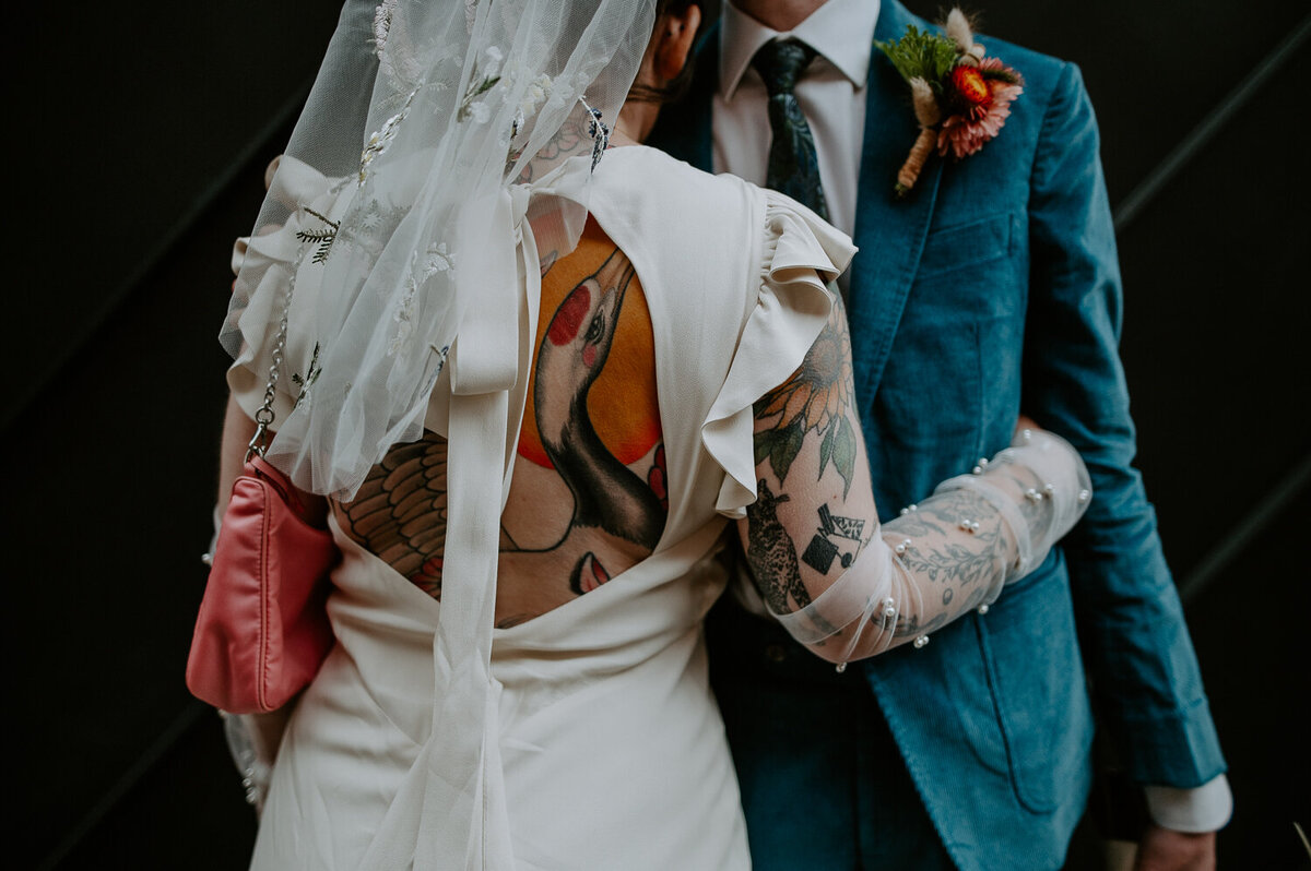 A bride shows her large tattoo on her back through a backless wedding dress.