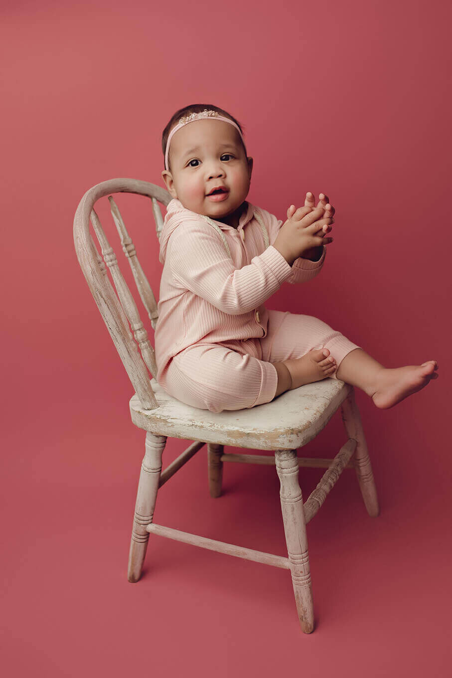 a one year old girl sitting on a white chair in rochester ny clapping her hands