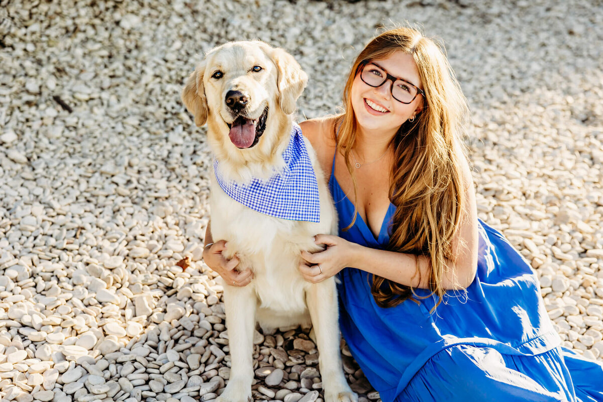 gorgeous teen girl in a bright blue dress sitting next to her dog on a white stone beach captured by Green Bay senior photographer Ashley Kalbus