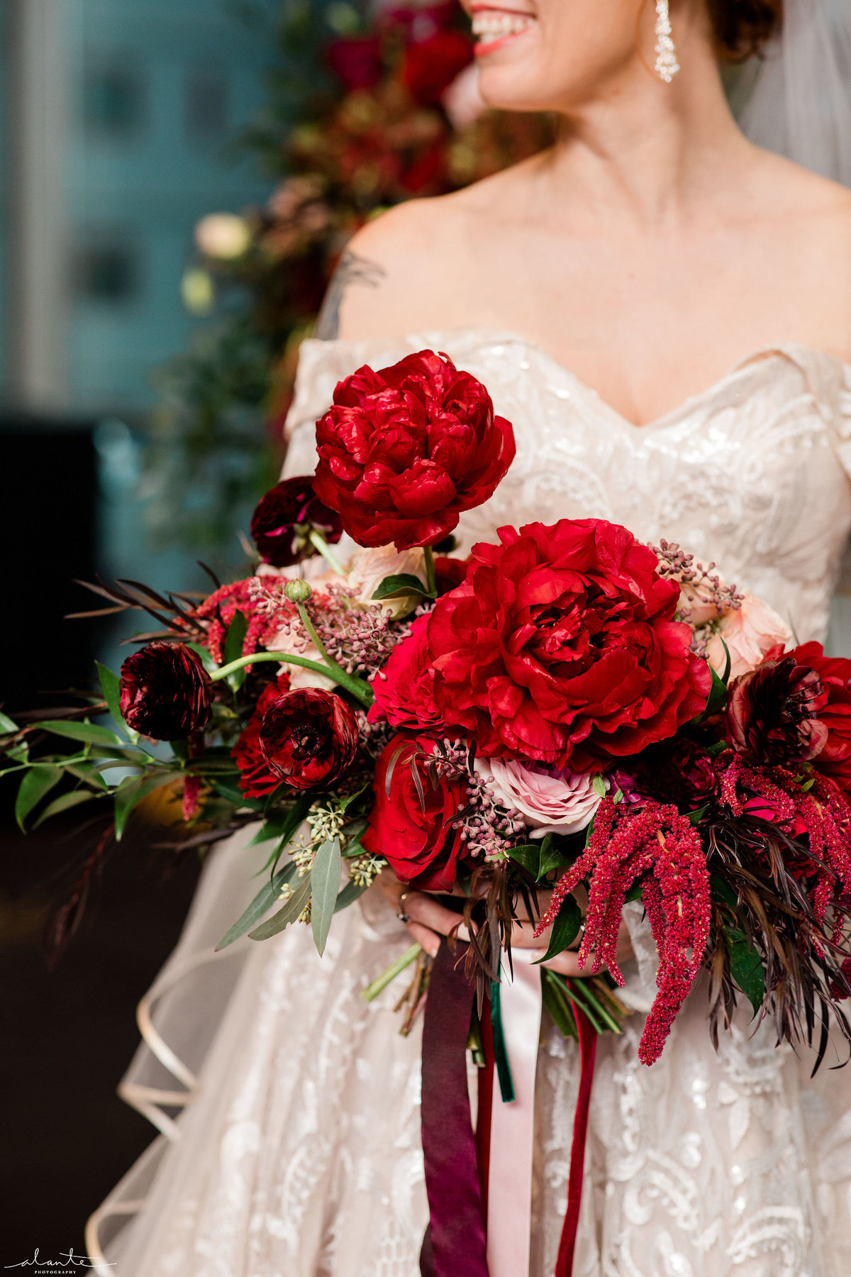 Bride holding bouquet of red peonies, red amaranthus, roses, and ranunculus, with ribbon streamers