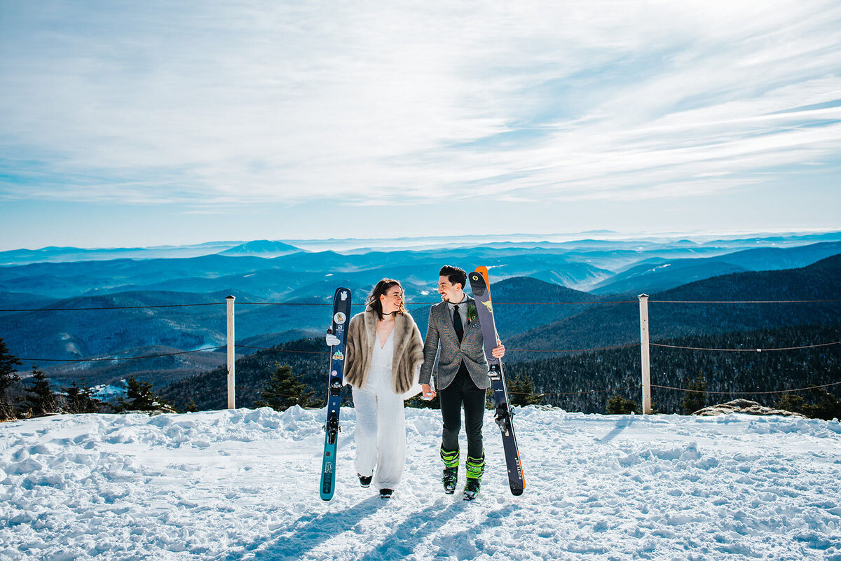 couple walking with skis on top of killington mountain at winter ski elopement