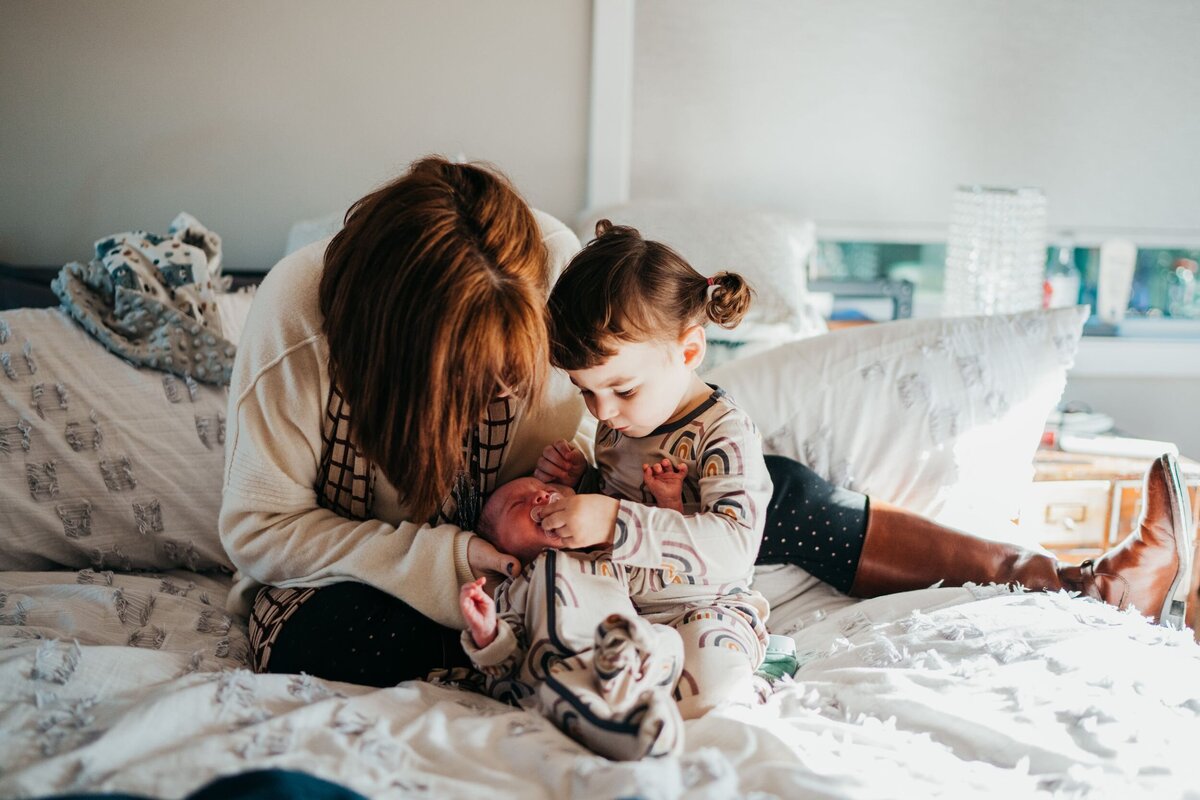 toddler-girl-help-mom-feed-newborn-sister