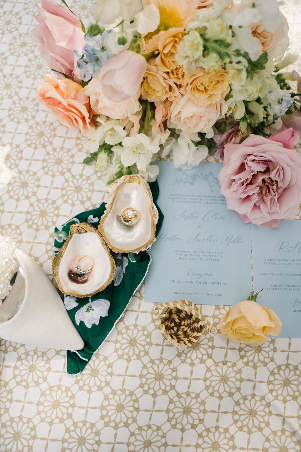 Flat lay of blue wedding stationery with florals and oyster shells holding the wedding rings