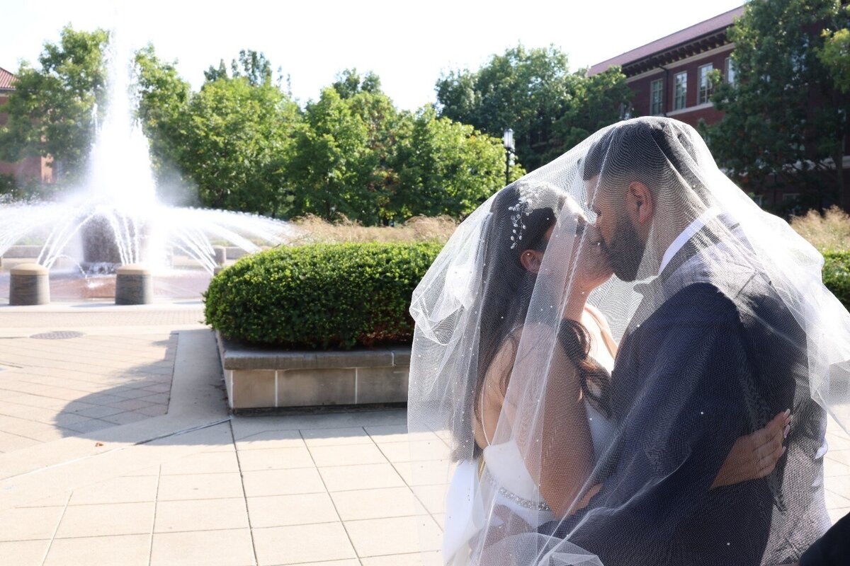 Bride and groom kiss passionately in front of water fountain