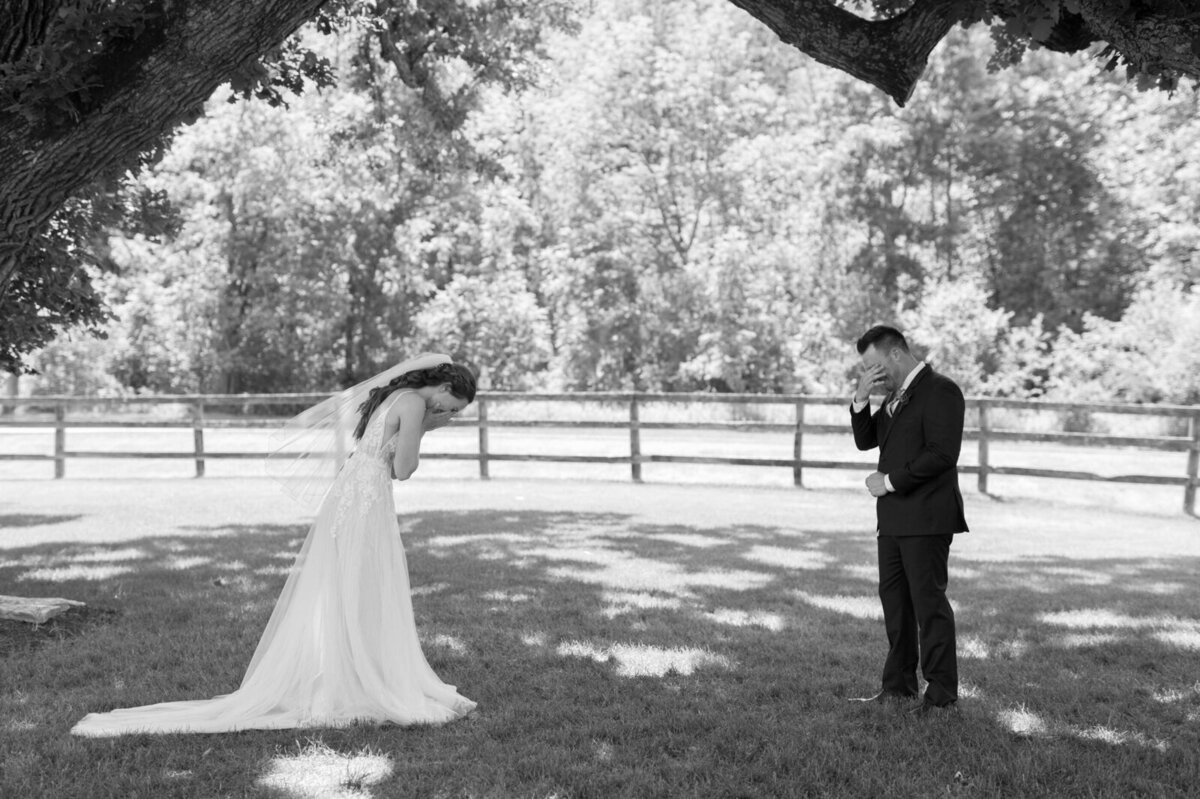 black and white image of bride and groom outside covering their eyes before first looks on their wedding day taken by tom thornton photography in minnesota