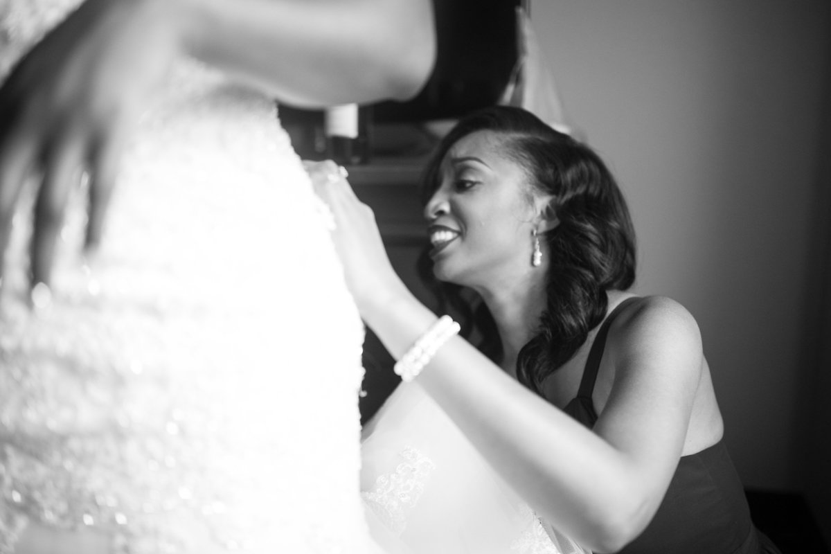 Black and white, close up image of the maid of honor helping the bride get into her wedding gown.