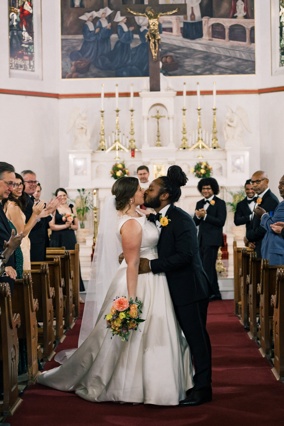 A couple stands in the aisle of a lavish catholic church and shares a first kiss.
