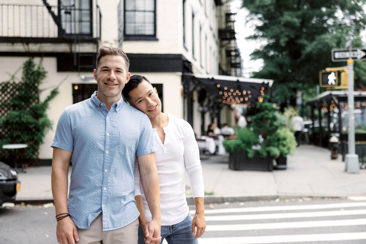 The engaged man is leaning his head on his fiancé's shoulder in the middle of a street in West Village, NYC. Image by Jenny Fu Studio