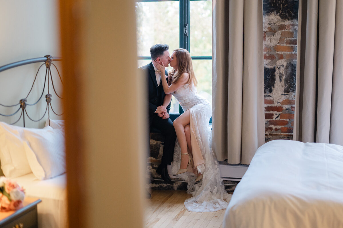 Photo capturée sur le vif dans un style paparazzi des mariés qui s’embrassent tendrement dans leur chambre d’hôtel du Vieux-Montréal, moment intime et moderne reflétant l’élégance urbaine d’un mariage en ville