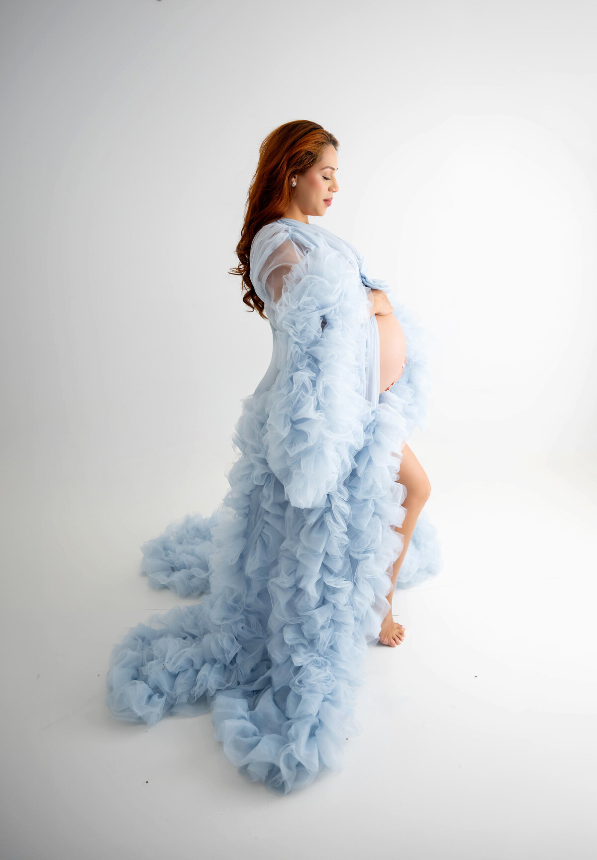 With a slight smile on her face, pregnant women wearing a baby blue couture robe looks down at her baby bump.