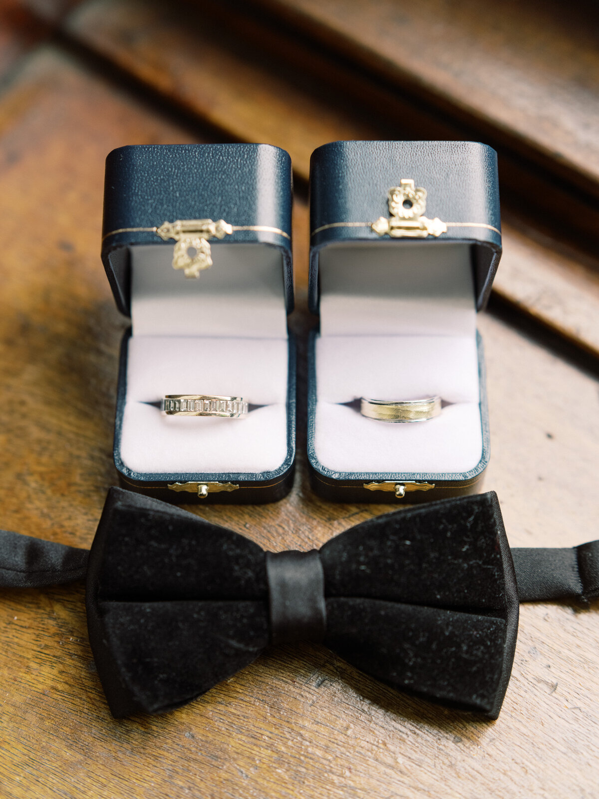 Two wedding bands elegantly displayed in stylish blue cases alongside a classic bow tie, capturing the essence of love and commitment in a refined manner.