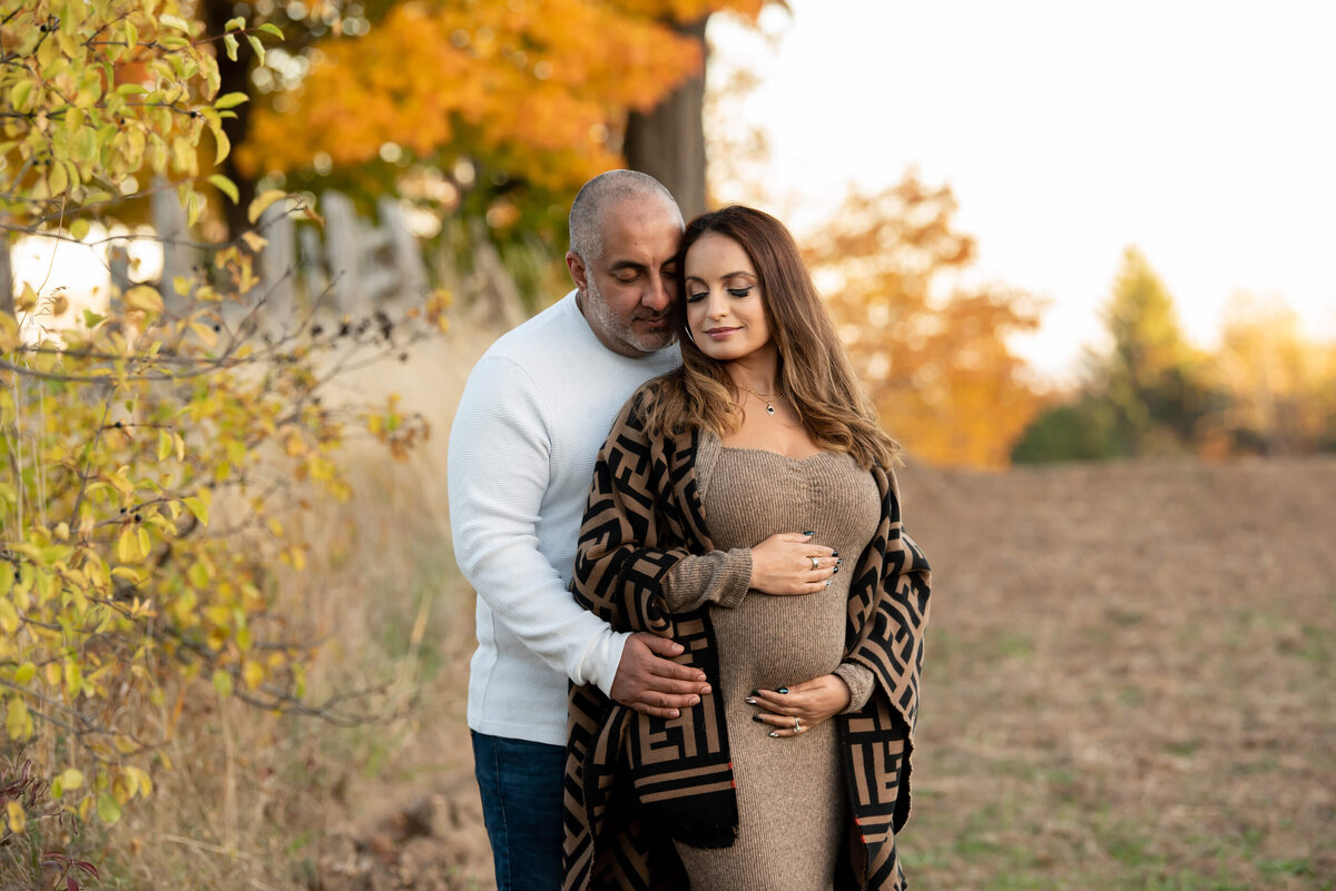 husband hugging wife's belly from behind for their fall Toronto maternity photos