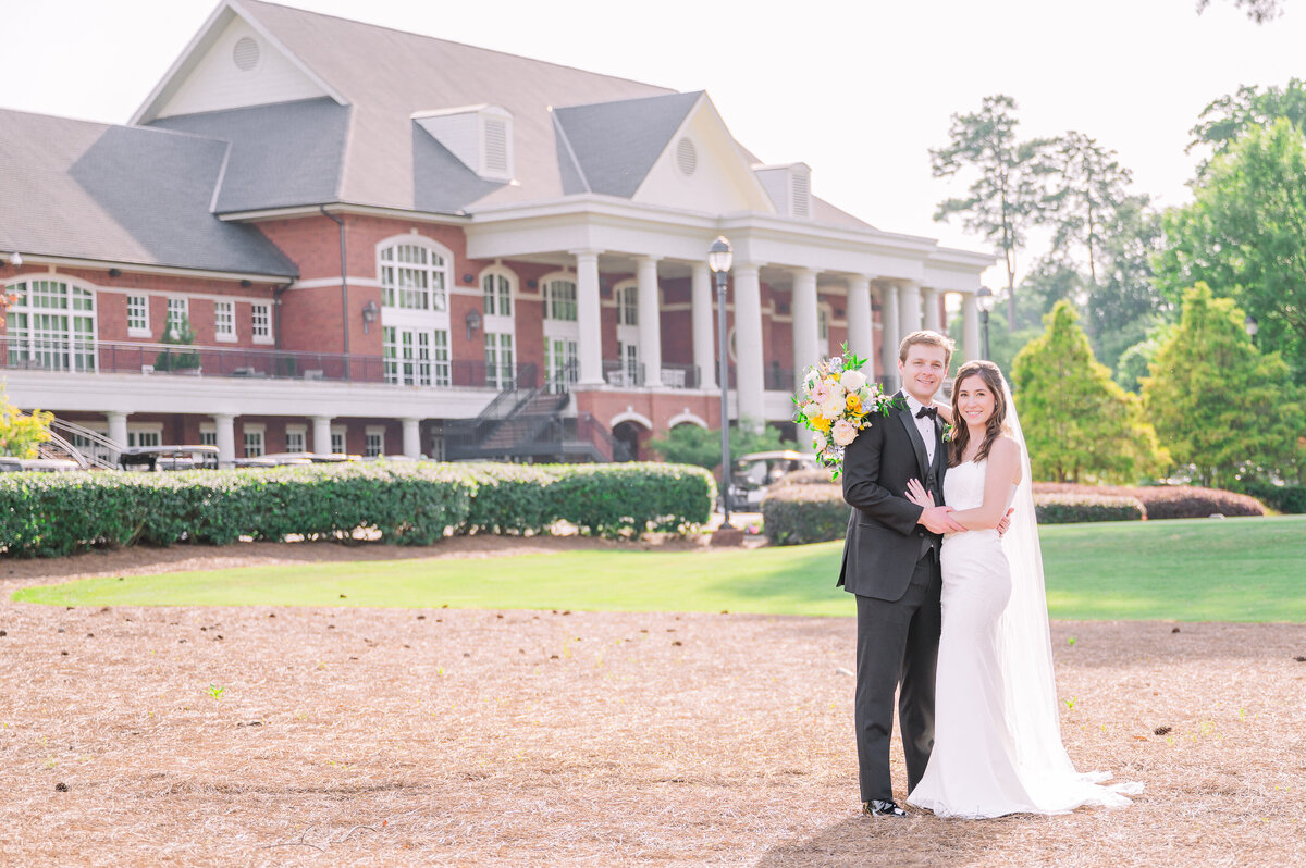 A happy couple standing in front of The Prestonwood Country Club at sunset in June enjoying their destination wedding photos 