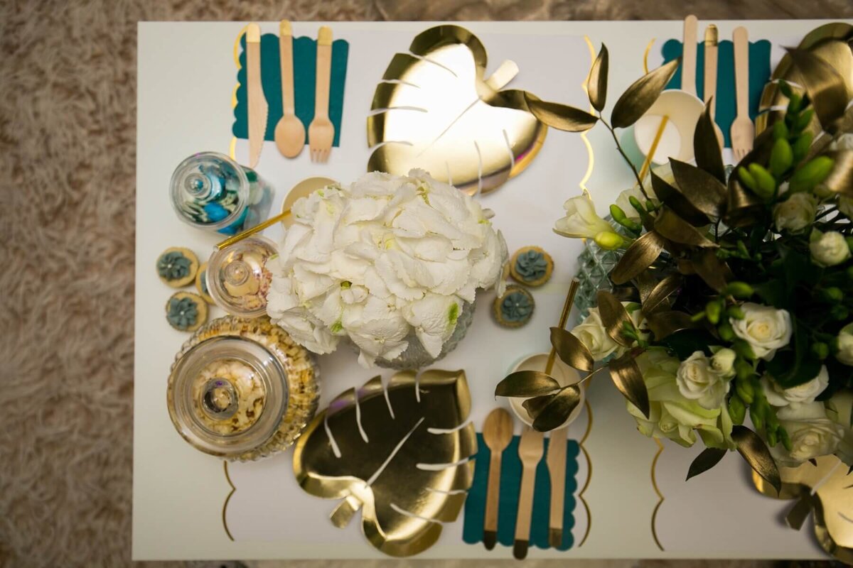 Gold and white children's table setting with sweet jars, flowers and gold leaf plates