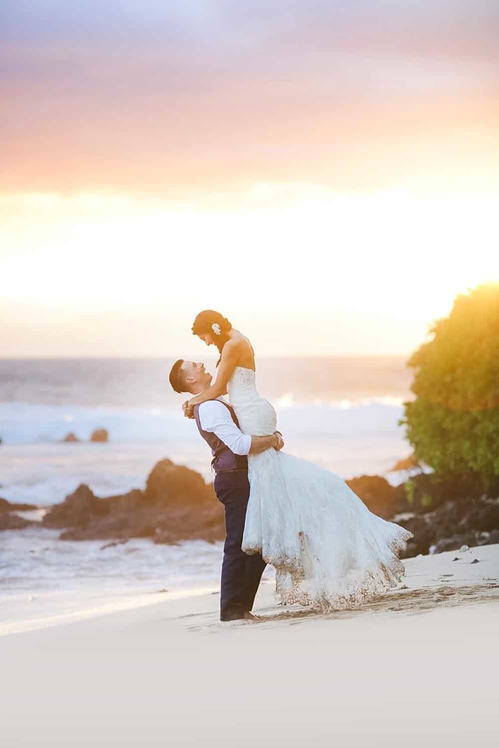 Excited couple having their honeymoon portraits taken on Maui by Love + Water dance at sunset next to the ocean