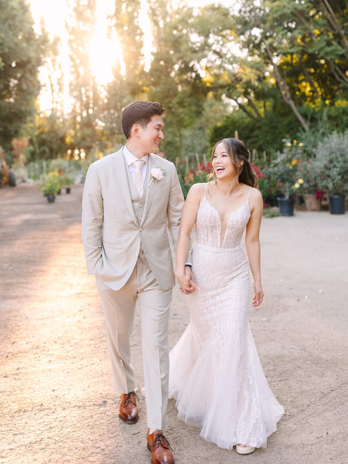 A couple walks hand in hand down a sunlit path, surrounded by blooming flowers and greenery, radiating love and joy.